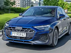 Młody kierowca w czapce za kierownicą granatowego Audi A3, jadącego po miejskiej drodze.