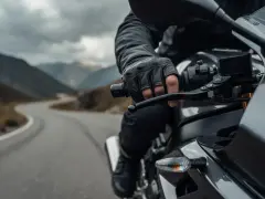 Motocyklista w skórzanej rękawicy trzyma kierownicę, gotowy do zmiany biegu. Droga wijąca się przez górzysty krajobraz.