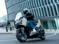 Mężczyzna w kasku jedzie skuterem Yamaha X-MAX 125 po mieście. Czy to lepszy wybór niż Honda Forza 125?