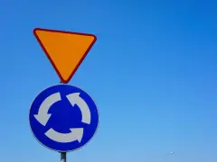 Znak podporządkowania (ustąp pierwszeństwa) i znak ronda na tle błękitnego nieba.