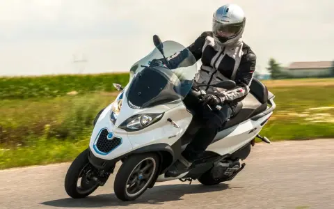 Biały Piaggio MP3 500 z kierowcą w kasku pędzi po drodze. Zastanawiasz się nad jego spalaniem?