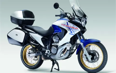 Honda Transalp 700 dane techniczne: turystyczny motocykl z kuframi, biało-niebieski, złote felgi, gotowy na przygodę.