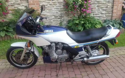 Klasyczny motocykl Yamaha XJ 900 w kolorze białym i granatowym, z niebieskimi i żółtymi pasami, zaparkowany na brukowanym podjeździe.