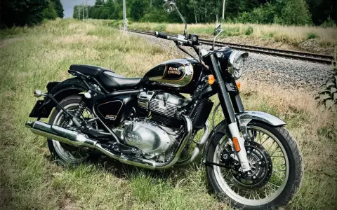Czarny Royal Enfield Classic 650 lśni chromem na tle torów kolejowych i zieleni. Gotowy na przygodę.