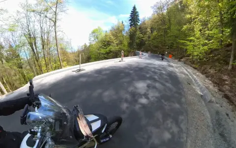 Motocyklista pokonuje zakręty na malowniczej drodze stu zakrętów, otoczonej zielonymi lasami.