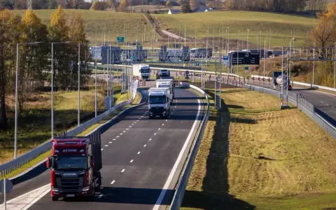 Ciężarówki na Via Baltica w jesiennym krajobrazie. Droga szybkiego ruchu z wieloma pojazdami, w tym czerwonym Scanią.