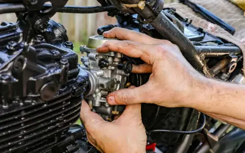 Dłonie mechanika regulują gaźnik motocykla, kluczowy element odpowiedzialny za symbol ssania paliwa i powietrza.