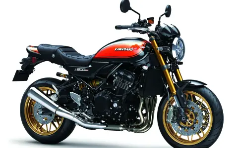 Stylowy czarny motocykl Kawasaki Z900RS z pomarańczowo-żółtym malowaniem na baku i złotymi felgami.