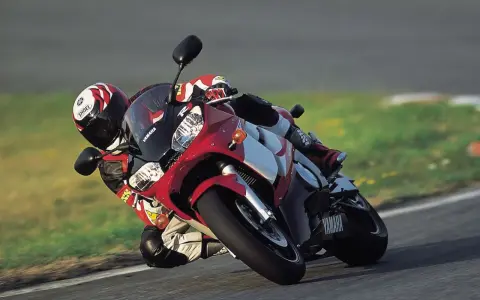 Motocyklista na torze pochyla się na swoim czerwono-białym motocyklu Yamaha R6 2001, w pełni ubrany w kombinezon i kask.