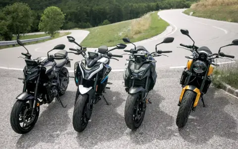Cztery motocykle typu naked stojące na zakręcie górskiej drogi.