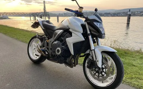 Biały motocykl Honda CB1000R, model a2 motor, zaparkowany nad rzeką o zachodzie słońca.