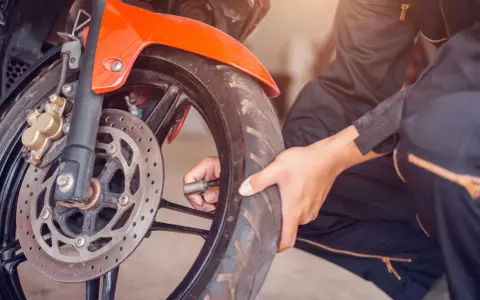 Sprawdzanie, jakie ciśnienie w oponach motocykla jest kluczowe dla bezpieczeństwa. Dłoń z manometrem przy wentylu przedniego koła.