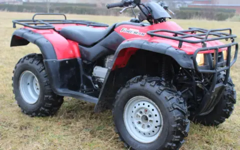 Czerwony quad Honda TRX 350 Foreman gotowy do jazdy po nierównym terenie.