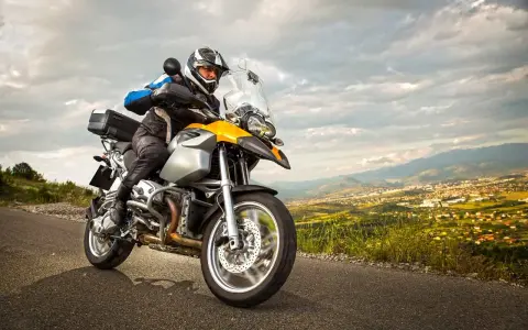 Motocyklista w kasku jedzie na motocyklu turystycznym. W tle rozciąga się malowniczy krajobraz z miastem. Zastanawiasz się nad koszt przerejestrowania motocykla?