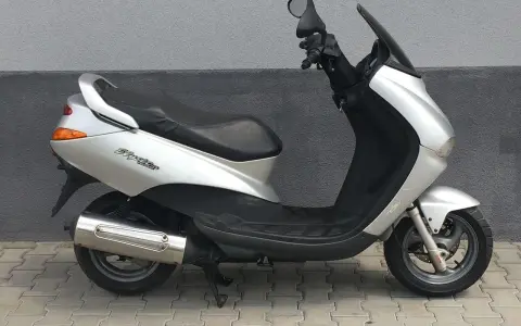 Srebrny skuter Peugeot Elyseo 125 z czarnym siedzeniem i przyciemnianą szybą, zaparkowany na chodniku.