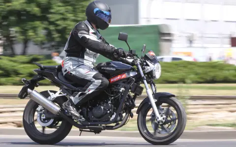 Motocyklista w kasku i kombinezonie jedzie na czarnym motocyklu Hyosung GT 125.