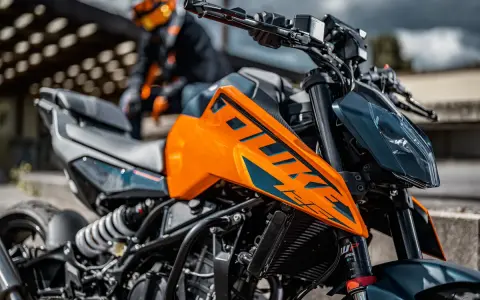 Pomarańczowy KTM Duke 390, zarejestrowany na 125, z motocyklistą w tle. Gotowy na przygodę!