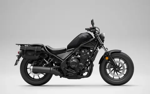 Czarny motocykl Honda Rebel 500 z sakwami, gotowy na podróż. Jego prędkość maksymalna pozwala na swobodne pokonywanie tras.