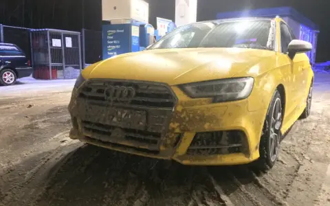 Żółte Audi na stacji benzynowej, pokryte błotem i śniegiem. Nieczytelna tablica rejestracyjna utrudnia identyfikację.