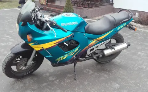 Turkusowy Suzuki GSXF 600 z żółto-fioletowymi grafikami, zaparkowany na kostce brukowej przed domem.