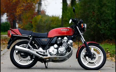 Klasyczny motocykl Honda CBX 1000 w kolorze czerwonym, z widocznym potężnym silnikiem i chromowanymi elementami, zaparkowany na tle jesiennej zieleni.