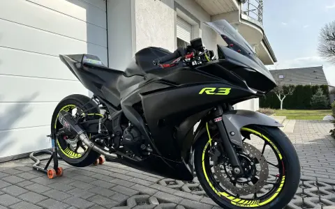 Czarny motocykl Yamaha R3 z żółtymi akcentami na felgach i owiewkach. Widać sportowy wydech Yoshimura. Idealny do poznania yamaha r3 dane techniczne.