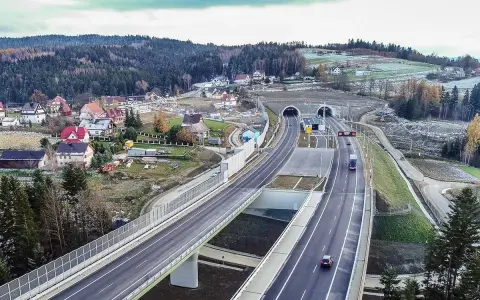 Nowa zakopianka trasa z tunelami i wiaduktami, otoczona lasami i zabudowaniami.