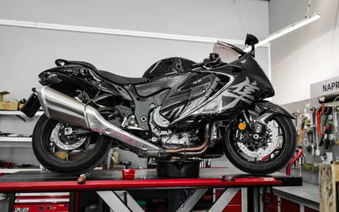 Czarny, lśniący motocykl typu naked bike na podnośniku w warsztacie. W tle tablica z narzędziami i napis "NAPRAWA".