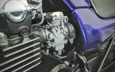 Szczegółowy widok gaźnika motocyklowego, kluczowego elementu układu dolotowego, z widocznymi przewodami i częściami silnika.