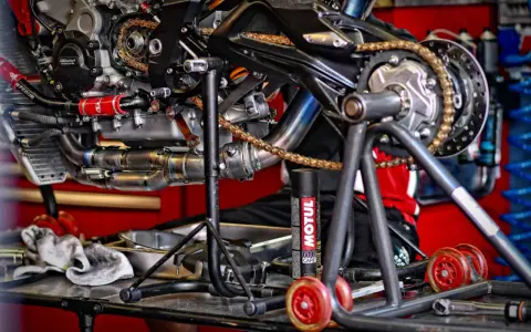 Motocykl na stojaku, widoczny napęd i łańcuch. Puszka smaru Motul sugeruje, co ile smarować łańcuch w motocyklu.