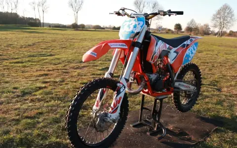 Pomarańczowy motocykl KTM SX 125 na stojaku, gotowy do jazdy. Zastanawiasz się, ile koni ma KTM SX 125? Ten model to potęga na torze!