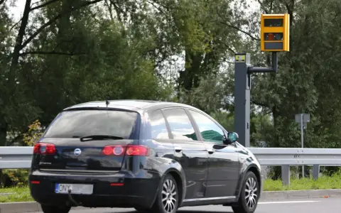 Czarny samochód mija fotoradar. Kierowca motocykla powinien uważać na ograniczenie prędkości.