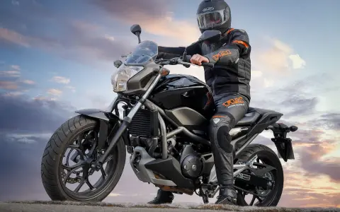 Motocyklista w kasku i kombinezonie siedzi na czarnym motocyklu. Idealny motor na kat B, gotowy na przygodę.