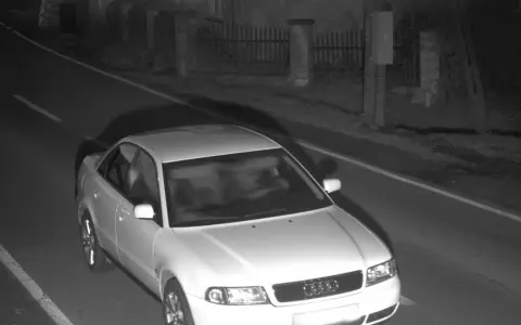Biały sedan Audi przejeżdża przez nocne zdjęcie z fotoradaru.