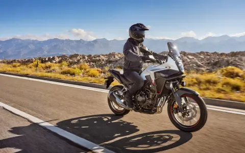 Motocyklista na białym Honda CB500X przemierza malowniczą, górską drogę.
