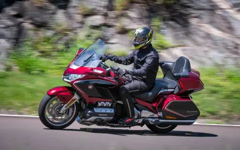 Mężczyzna w kasku jedzie lśniącym, czerwonym motocyklem Honda Gold Wing, uznawanym za najlepszy motocykl turystyczny.