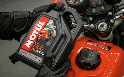 Rękawice motocyklisty trzymają olej Motul 7100 10W-40. Pytanie: co ile wymieniać olej w motocyklu?