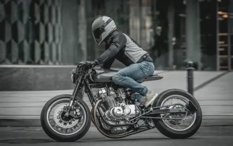 Motocyklista w kasku i jeansach pędzi na stylowym Suzuki GS 650 po miejskiej ulicy.
