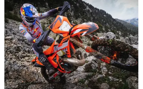 Motocyklista w kasku Red Bull na pomarańczowym KTM EXC 300 2T pokonuje kamienisty teren. Dane techniczne tego potwora terenowego są imponujące.