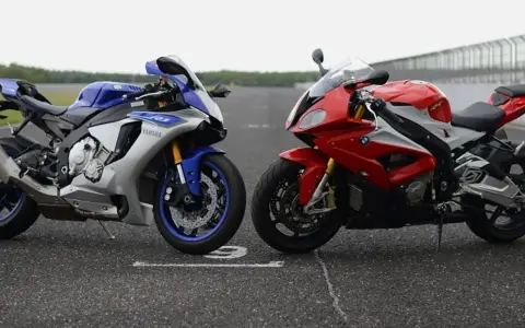 Dwa sportowe motocykle: niebiesko-srebrny Yamaha R1 i czerwono-biały BMW S1000RR 2020, stojące na torze wyścigowym.