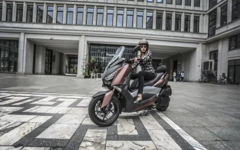 Kobieta na skuterze Yamaha X-MAX 300, gotowa do jazdy. Zastanawia się, jaka będzie jej prędkość maksymalna w mieście.