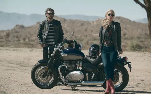 Para w skórzanych kurtkach pozuje przy motocyklu Triumph Speedmaster na pustynnym tle.