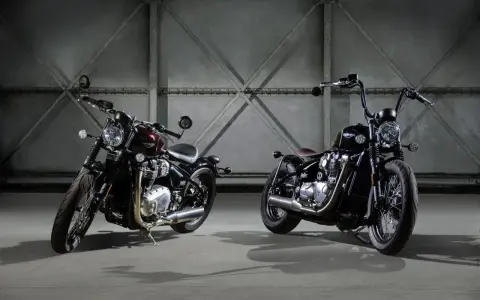 Dwa motocykle Triumph Bonneville Bobber w ciemnych kolorach, stojące obok siebie w industrialnym wnętrzu.