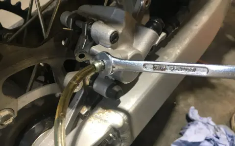 Klucz nasadowy odkręca odpowietrznik podczas czyszczenia hamulców motocykla. Płyn hamulcowy spływa przez przezroczysty wężyk.