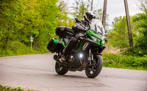 Motocyklista na zielonym Kawasaki Versys 1000, z kuframi, pokonuje zakręt. Nawet z potencjalnymi wadami, jazda nim to przygoda.