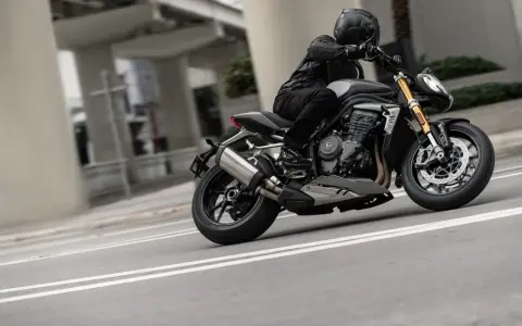 Motocyklista w kasku i skórzanej kurtce pochyla się na swoim motocyklu Triumph Speed Triple, pokonując zakręt na miejskiej drodze.