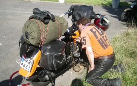 Motocyklista sprawdza uszkodzony gaźnik objawy. Na motocyklu sakwy, zielony worek i czarne rękawice.