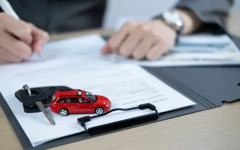 Na stole leżą kluczyki i czerwony samochodzik, a ktoś podpisuje dokumenty. To może być dowód rejestracyjny tymczasowy.