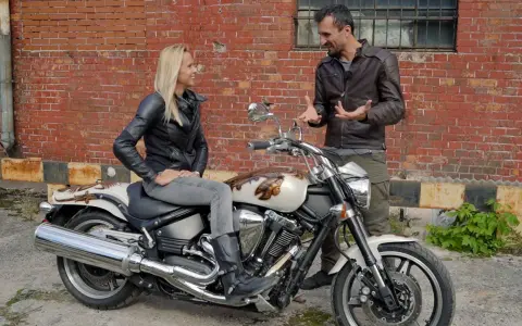 Kobieta siedzi na motocyklu Yamaha Warrior 1700, mężczyzna obok opowiada o jego możliwościach.