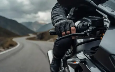 Motocyklista w skórzanej rękawicy trzyma kierownicę, gotowy do zmiany biegu. Droga wijąca się przez górzysty krajobraz.